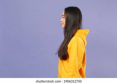 Side View Of Smiling Beautiful Young Brunette Asian Woman Wearing Casual Basic Yellow Hoodie Standing Holding Hands Crossed Looking Camera Isolated On Pastel Violet Colour Background Studio Portrait