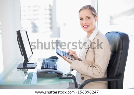 Side view of smiling blonde businesswoman using calculator in bright office