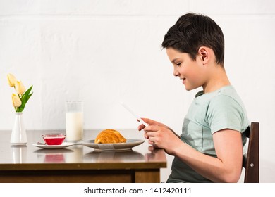 side view of smiling boy using digital tablet during breakfast in kitchen