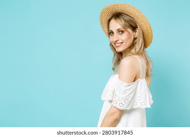 Side view of smiling charming pretty cute beautiful young blonde woman 20s wearing white summer dress hat standing looking camera isolated on plain pastel light blue cyan background studio portrait