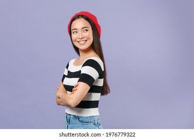 Side View Of Smiling Cheerful Pretty Young Brunette Asian Woman In Striped T-shirt Red Beret Standing Holding Hands Crossed Looking Aside Isolated On Pastel Violet Colour Background Studio Portrait