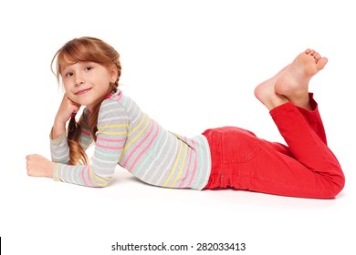 Side View Of Smiling Child Girl Lying On Stomach On The Floor With Crossed Legs, Over White Background 