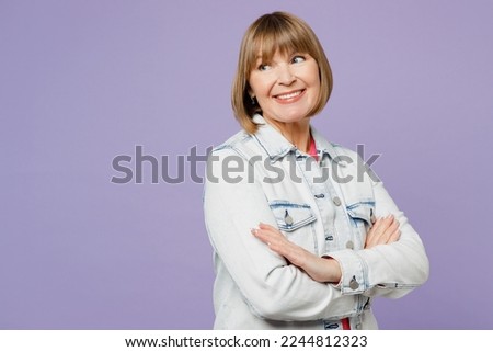Side view smiling elderly blonde woman 50s years old she wear casual clothes denim jacket t-shirt hold hands crossed folded look aside on area isolated on plain pastel light purple background studio