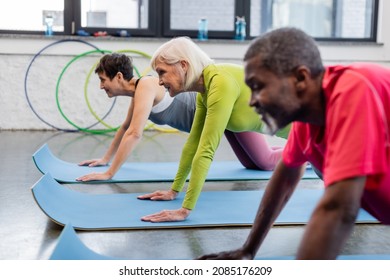 Side view of smiling elderly woman exercising near multiethnic people in sports center - Powered by Shutterstock