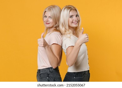 Side View Of Smiling Family Two Women Blonde Mother Daughter Wearing Casual Clothes Standing Back To Back Showing Thumbs Up Looking Camera Isolated On Bright Yellow Colour Background Studio Portrait