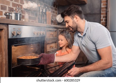 'Side view of smiling father and daughter taking cake from oven