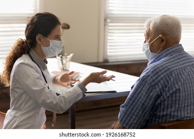 Side view smiling female doctor wearing protective face mask consulting old man at meeting in hospital, physician therapist and senior patient discussing medical checkup results, healthcare concept