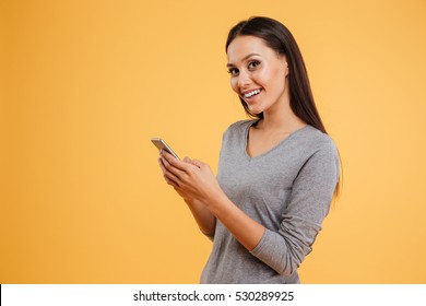 Side view of smiling girl with phone in stodio. girl looking at phone. isolated orange background