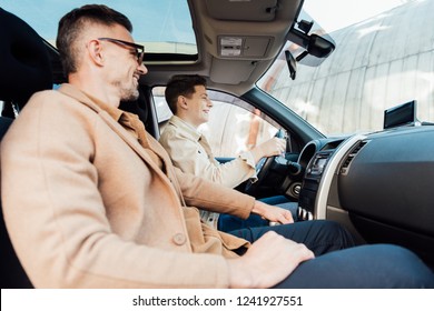 Side View Of Smiling Handsome Father Teaching Teen Son Driving Car