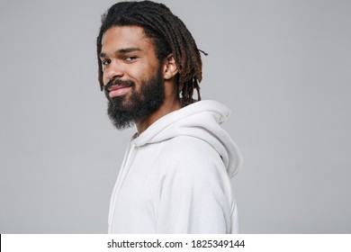 Side View Of Smiling Handsome Young African American Man With Dreadlocks 20s Wearing White Casual Streetwear Hoodie Posing Looking Camera Isolated On Grey Color Wall Background Studio Portrait