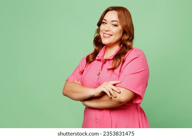 Side view smiling happy cheerful young chubby overweight redhead woman wear casual clothes pink dress hold hands crossed folded isolated on plain pastel light green color background. Lifesyle concept