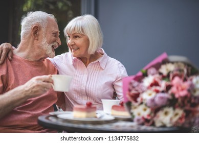 Side view of smiling loving couple drinking tea outside. They are hugging and looking at each other with care and sincere feelings - Powered by Shutterstock