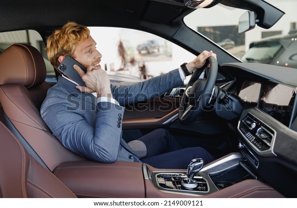 Side view smiling man driver male cabdriver\
wearing classic grey suit drive car hold wheel speak by mobile cell\
phone in traffic jam test auto want buy new automobile vehicle Sale\
transport concept.