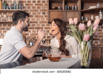 'side view of smiling man feeding woman with cake in kitchen - Shutterstock ID 600283082