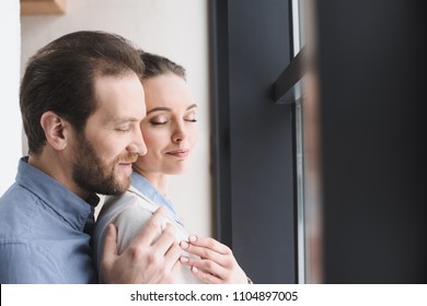 side view of smiling man hugging beautiful wife
