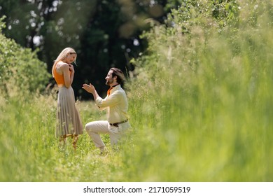 Side View Of Smiling Man Pointing At Stylish Girlfriend While Kneeling On Lawn In Park