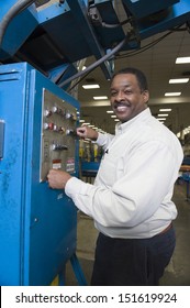 Side view of a smiling man working on control panel in the newspaper factory