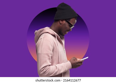 Side view smiling millennial black guy in pink hoodie  hat   shades using mobile phone  checking social media  sending message against purple background and colorful gradient circle