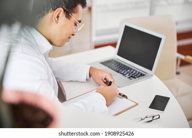 Side View Of A Smiling Optician Leaning Over A Blank Sheet Of Paper On The Desk