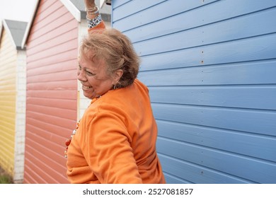 Side view of smiling senior woman with hand raised against beach hut - Powered by Shutterstock