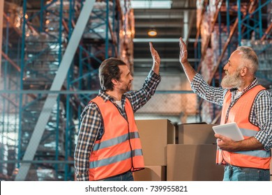 Side View Of Smiling Warehouse Workers Giving High Five While Working With Digital Tablet