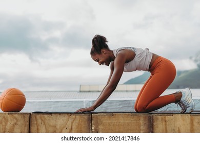 Side view of a smiling woman doing workout outdoors with a basketball in front. Sportswoman practicing yoga on rooftop. - Powered by Shutterstock