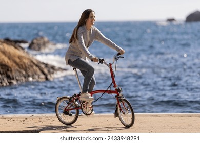 Side view of smiling woman riding an urban bicycle by the sea - Powered by Shutterstock