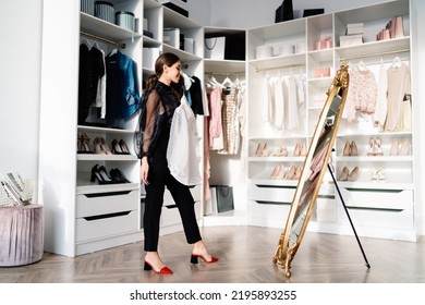 Side View Of Smiling Woman In Stylish Apparel Standing In Dressing Room Near White Closet And Looking At Reflection In Mirror While Dressing Up At Home