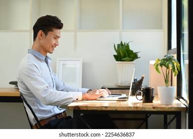 Side view of smiling young asian male investor analyzing financial online data on laptop computer - Shutterstock ID 2254636837