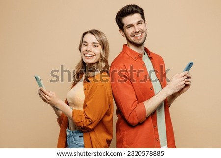 Side view smiling young couple two friends family man woman wear casual clothes hold in hand use mobile cell phone together stand back to back isolated on pastel plain light beige background studio