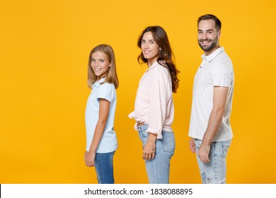 Side View Smiling Young Happy Parents Mom Dad With Child Kid Daughter Teen Girl In Basic T-shirts Looking Camera Isolated On Yellow Background Studio Portrait. Family Day Parenthood Childhood Concept