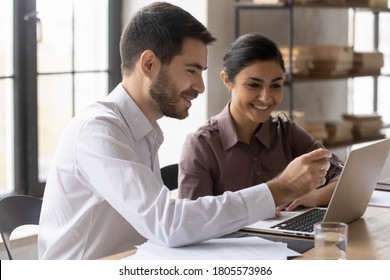 Side View Smiling Young Male Manager Pointing At Computer Screen, Explaining Corporate Software Or Working On Online Project With Happy Mixed Race Indian Female Colleagues At Brainstorming Meeting.