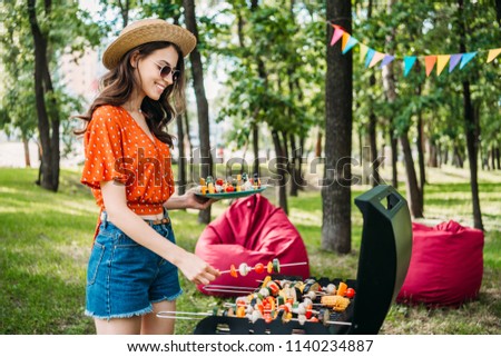 side view of smiling young woman taking vegetables from grill in park