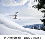 Side view snapshot of skier conducting extreme jump from a snowy slope, flying against amazing sky and mountain range on background. Copy space. Concept of skiing and winter sport activities.