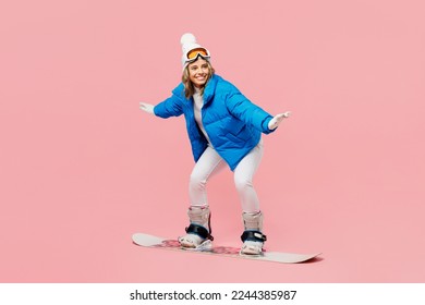 Side view snowboarder sportive fun woman wear blue suit goggles mask hat ski padded jacket snowboarding isolated on plain pastel pink background. Winter extreme sport hobby weekend trip relax concept
