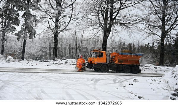 Side view of snowplow service truck - gritter\
car spreading salt on the road. Maintenance of roads in winter in\
the mountains.