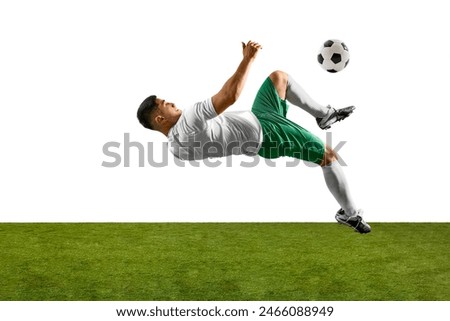 Side view of soccer player performing acrobatic kick with soccer ball in flight above him, against white background and green grass field. Professionals sport, competition, tournament, action concept