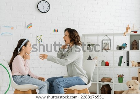 Side view of speech therapist opening mouth near pupil in consulting room
