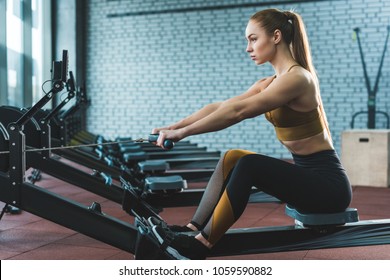 Side View Of Sportswoman Doing Exercise On Rowing Machine In Sports Center