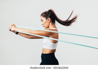 Side view of sportswoman exercising with resistance band against white wall - Shutterstock ID 2013622565