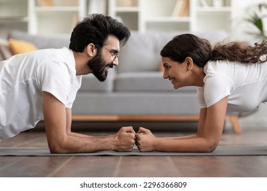 Side view of sporty indian couple making elbow plank exercise at home, romantic eastern spouses facing each other, having fun while doing domestic strength workout, enjoying healthy lifestyle - Powered by Shutterstock