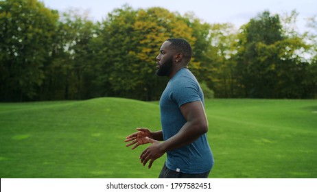 Side View Sporty Man Jogging In Green Park. Handsome Sportsperson Exercising Outdoors In Slow Motion. Male Runner Doing Cardio Workout On Road In Morning. African Man Running Outdoors