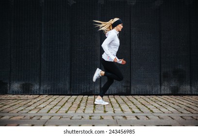 Side view of sporty young woman running on sidewalk in morning. Health conscious concept with copy space. - Shutterstock ID 243456985