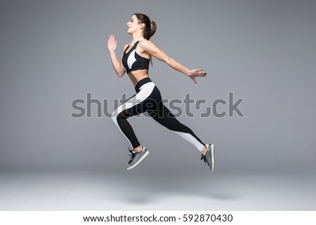 Side view of sporty young woman jumping isolated on grey background