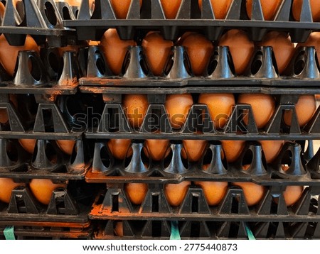 A side view of stacked black plastic trays housing fresh brown eggs in a warehouse or supermarket setting. This image showcases the efficiency of packaging and the massive scale of food distribution.