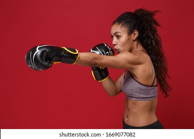 Side view of strong african american sports fitness boxer woman in sportswear working out isolated on red background. Sport exercise healthy lifestyle concept. Make boxing exercises in boxing gloves - Powered by Shutterstock