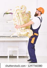 Side View Strong Bearded Man Carrying Old Armchair In Front Of Piano. Packing The Furniture And Moving To New Place.