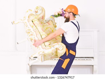 Side View Strong Bearded Man Carrying Old Armchair In Front Of Piano. Mover Walking With Fragile Old Piece Of Furniture In His Hands. Moving To New Place.