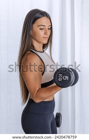Side view of strong female athlete doing bicep curls with heavy dumbbells during training at home