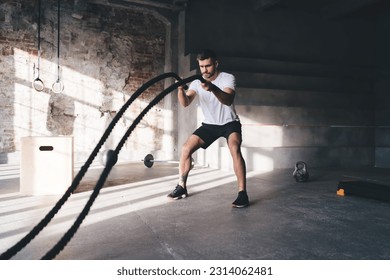 Side view of strong male athlete in sportswear battling ropes while training in gym and enhancing athletic power and working out - Powered by Shutterstock